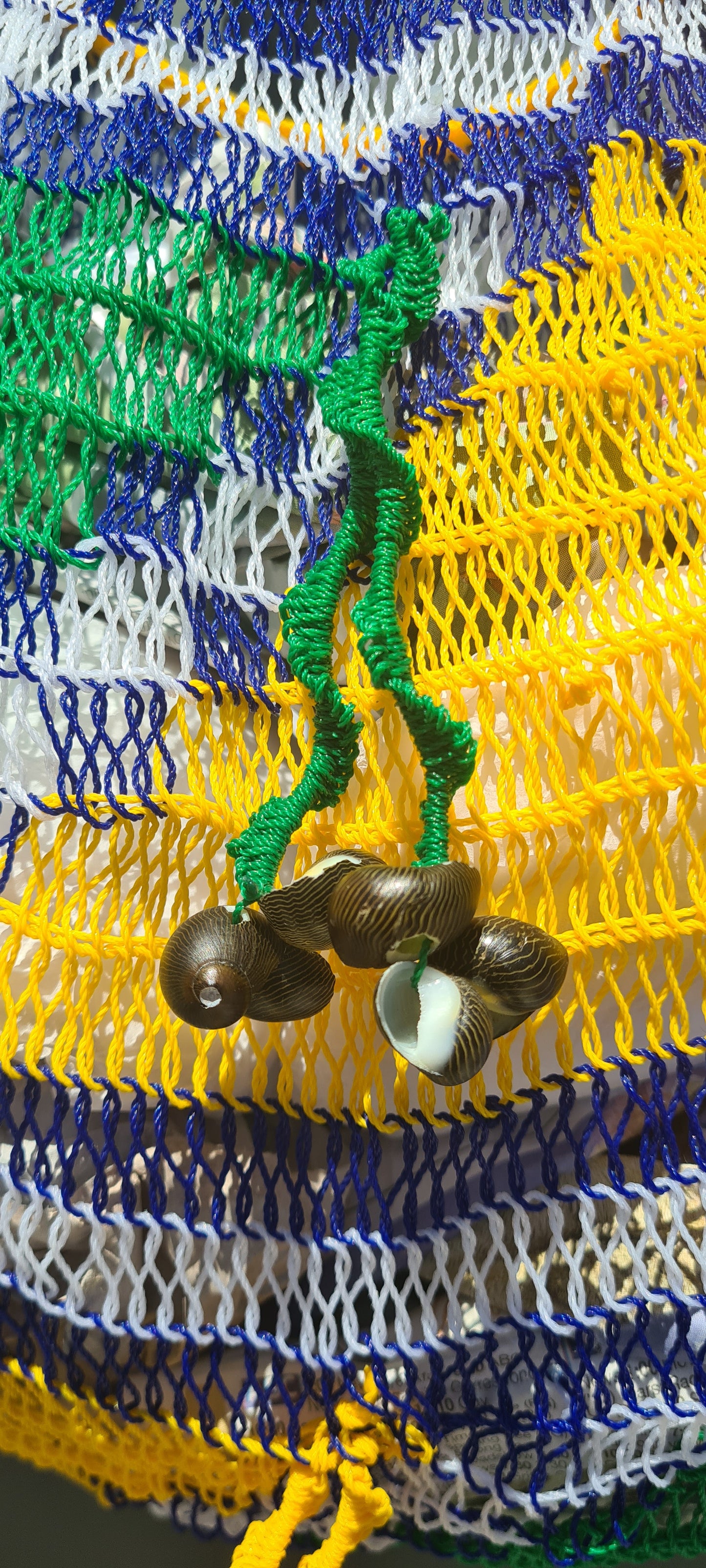 Handmade Morobe Nylon String Bilum Bag with Yellow and Green pattern on light background, Close up view of Green tassel and shells