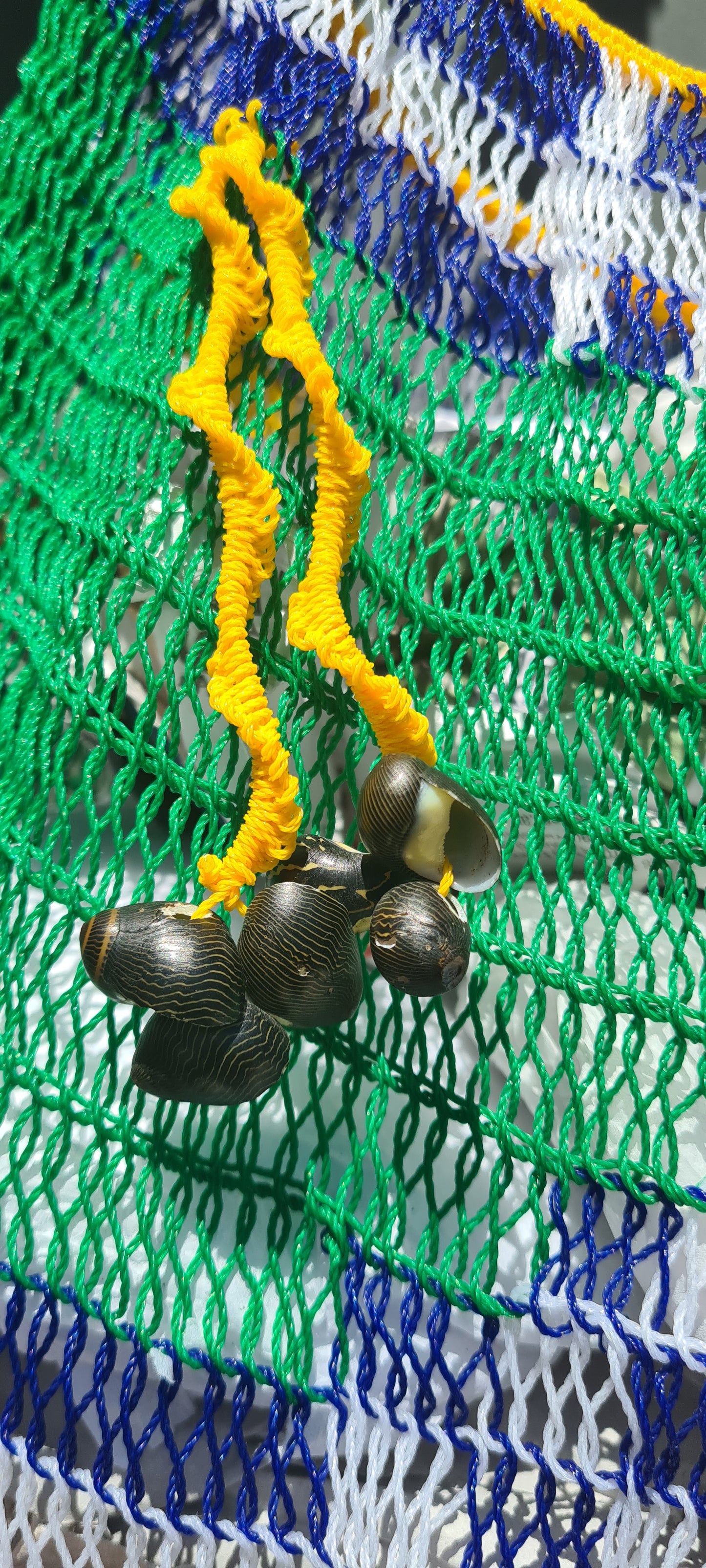 Handmade Morobe Nylon String Bilum Bag with Yellow and Green pattern on light background, Close up view of Yellow tassel and shells